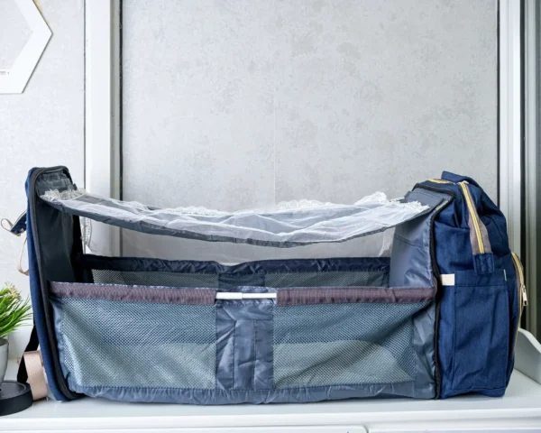 Foldable 2-in-1 diaper backpack opened into a portable baby bed with mesh sides, adjustable canopy support, and multiple storage compartments.