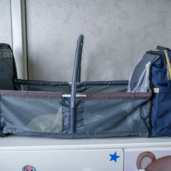 Foldable 2-in-1 diaper backpack opened into a portable baby bed with mesh sides, adjustable canopy support, and multiple storage compartments.