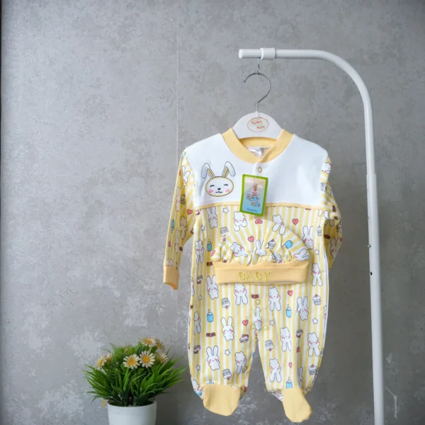 Yellow baby romper with bunny print and matching embroidered hat, displayed on hanger against a neutral wall with a decorative plant below.