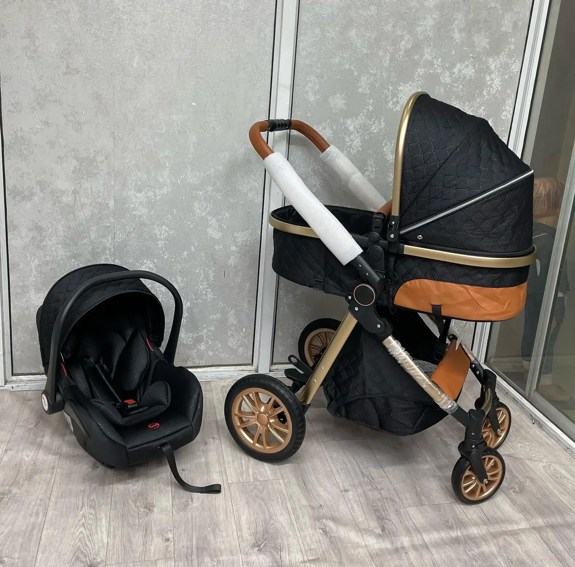 A stylish 3-in-1 premium baby stroller in black and gold, featuring a quilted design, adjustable handlebar, and durable wheels. Includes a detachable infant car seat for versatile use. Perfect for comfort, safety, and convenience.