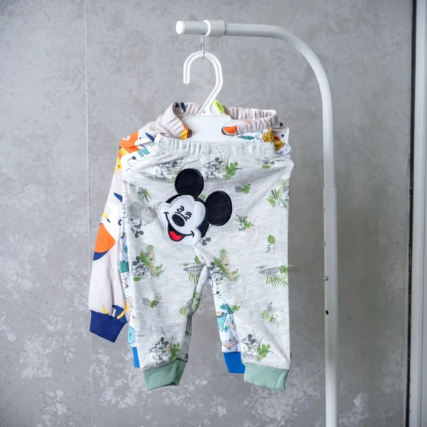 Set of baby trousers featuring grey pants with a Mickey Mouse patch, displayed on a hanger with colorful cartoon prints.