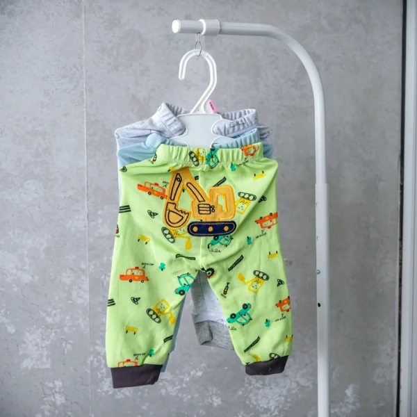 Set of baby trousers featuring green pants with a yellow excavator design and playful car prints, displayed on a hanger.