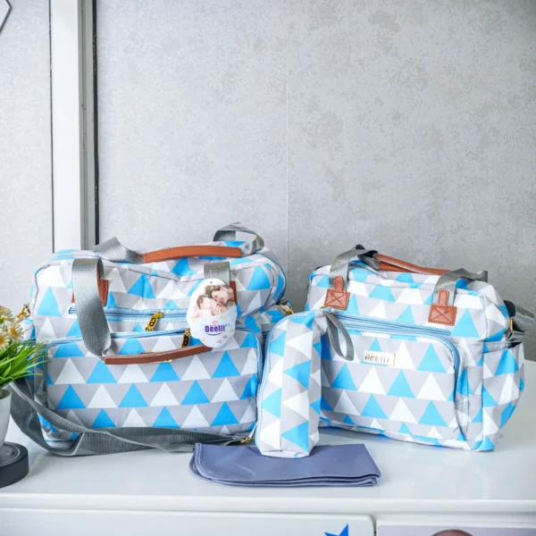 A set of blue and white geometric patterned diaper bags with gray and brown straps, including two bags, a bottle holder, and a changing mat, neatly arranged on a table.