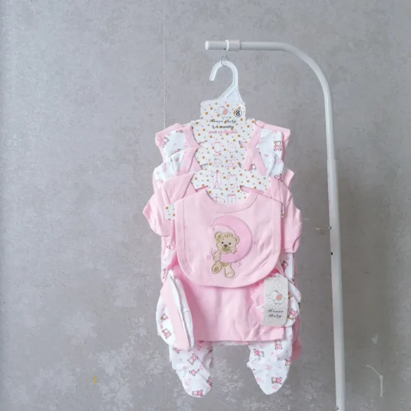 8-piece baby girl receiving set in soft pink with teddy bear embroidery, including bodysuit, bib, mittens, and footed pants.