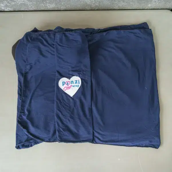 Three folded baby wrap carriers—light gray, navy blue, and dark green—are neatly displayed on a table, each with a heart-shaped logo reading "Ponzi Wrap".