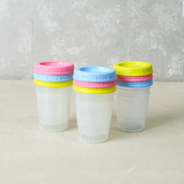 A set of three transparent baby food storage containers, each topped with bright, colorful lids (yellow, pink, and blue) stacked neatly together.