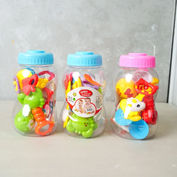Three clear rattle containers, each with a different mix of colorful baby toys, with alternating blue and pink lids, arranged side by side.
