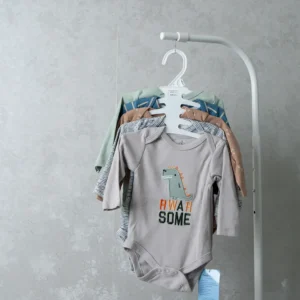 A set of baby bodysuits hanging on a white hanger, with the front onesie in light gray featuring a dinosaur and the text “Rwar Some.