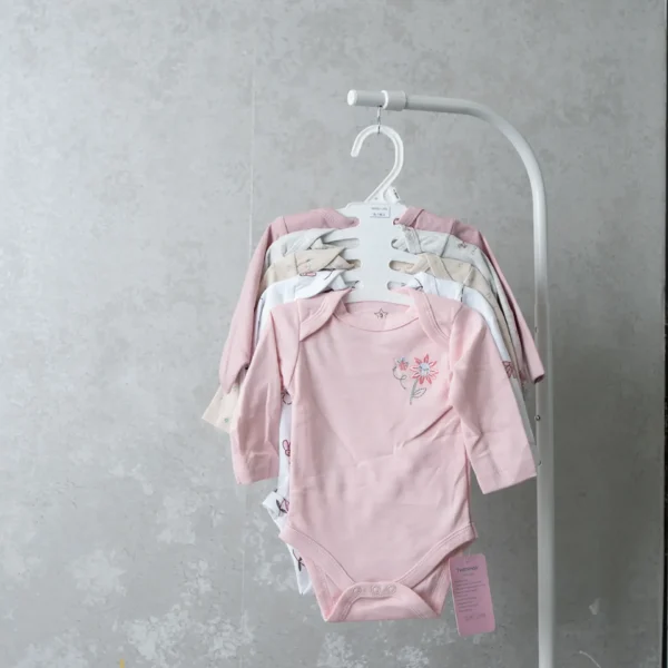 A collection of baby bodysuits on a hanger, with the front one in bright red featuring ladybugs and the text “mommy & me.