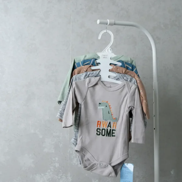 A set of baby bodysuits hanging on a white hanger, with the front onesie in light gray featuring a dinosaur and the text “Rwar Some.