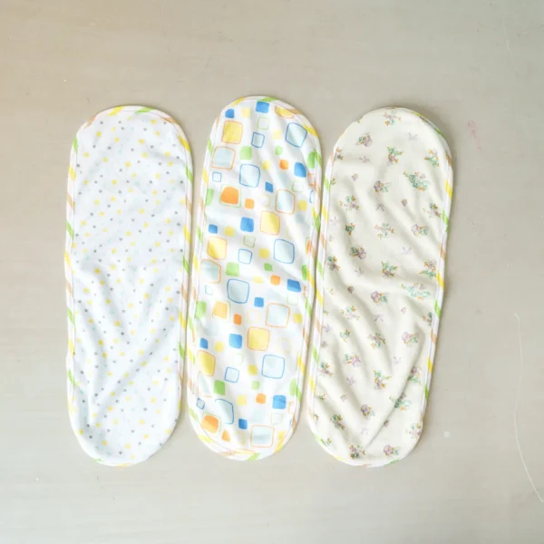 Three unfolded baby burp cloths with soft fabric and delicate patterns—yellow stars, colorful squares, and floral prints—laid flat on a surface.
