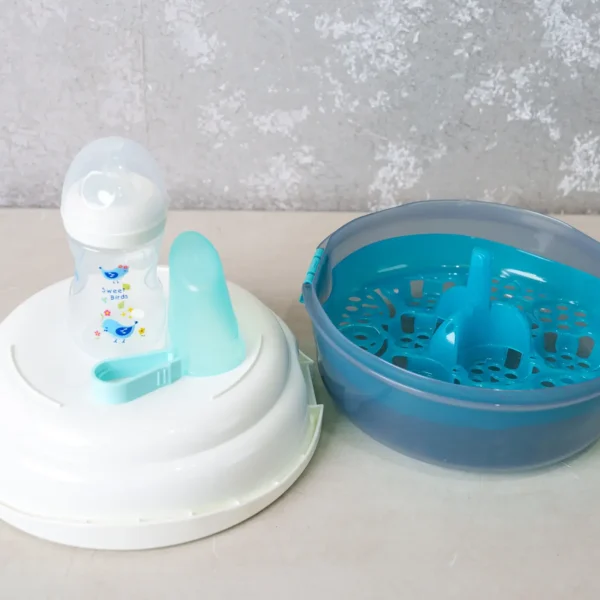 Open view of a microwave sterilizer showing internal compartments, a BPA-free baby bottle, and accessories on a clean surface.