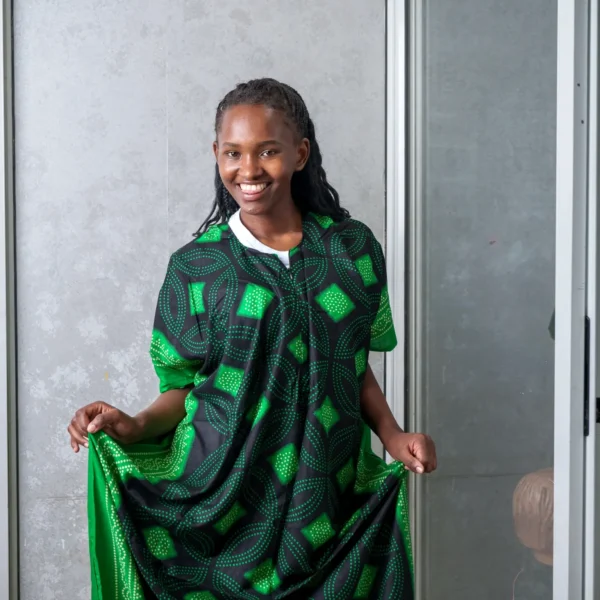 Woman dressed in a black nursing dera with green African-inspired patterns, smiling and displaying the wide, flowing cut of the outfit.